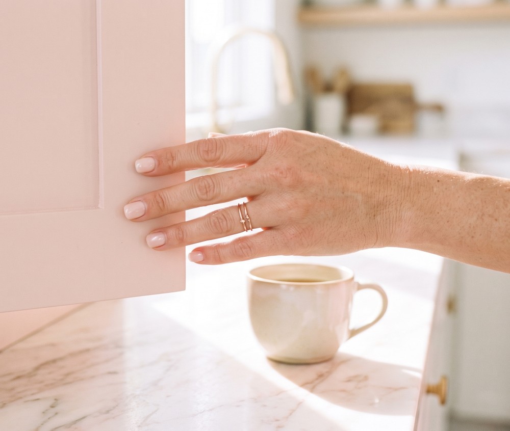 a woman’s hand using the pads of her index and middle fingers to gently, silently guide a pale pastel blush kitchen cabinet door shut